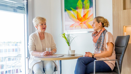 Komfortstation Bergmannsglück: Zwei Frauen sitzen sich an einem Tisch in einem schön dekorierten Patientenzimmer auf der Komfortstation gegenüber. Sie unterhalten sich.